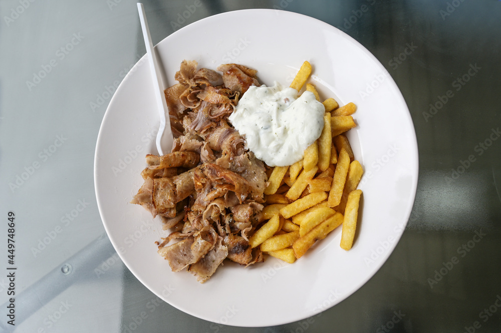 Doner kebab meat slices from rotating roasting spit with french fries and tzatziki yoghurt dip, served on a white plate in a turkish fast food restaurant, copy space, view from above