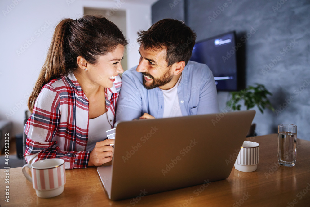 Smiling happy couple sitting at home and using tablet for online shopping.