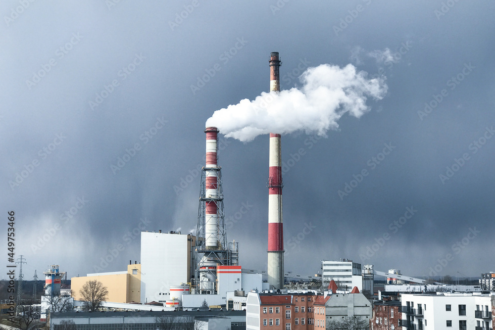 Thick white smoke comes out of a large chimney of an industrial facility or factory. Chimney against the blue sky. Environmental pollution