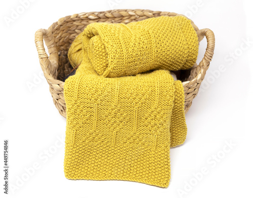 Yellow knitted blanket in diamonds pattern in basket on white background