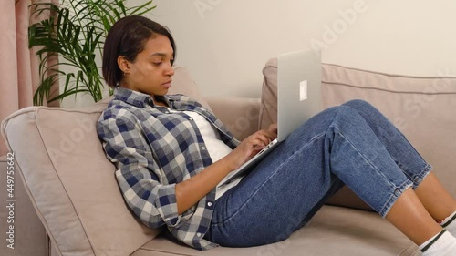 A young African-American woman is working at home online and has tipped her head over on the sofa from exhaustion. The concept of fatigue and stress, freelance.
