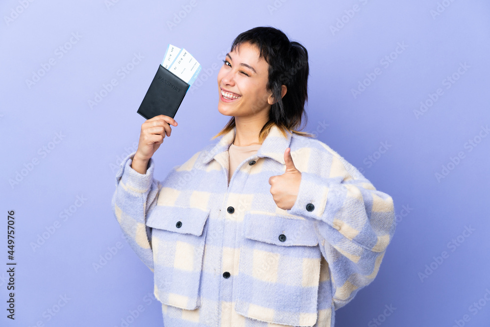 Young Uruguayan woman over isolated purple background in vacation holding a passport and plane with thumb up Young Uruguayan woman over isolated purple background in vacation holding a passport and plane with thumb up