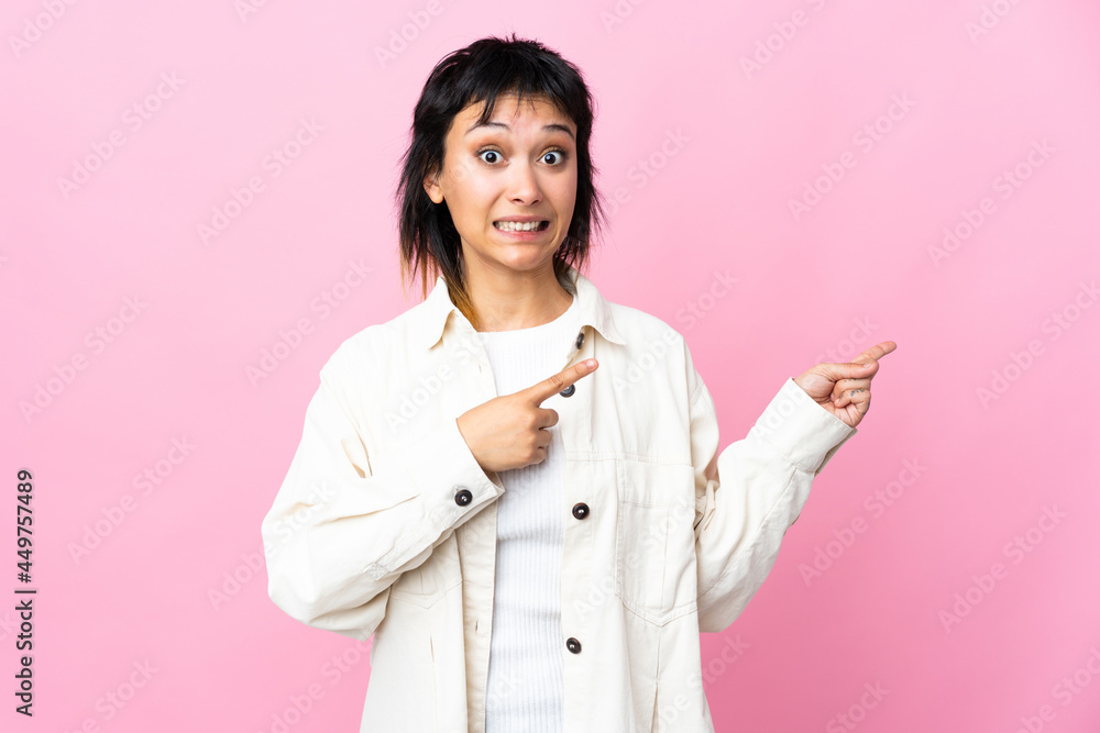 Young Uruguayan woman over isolated pink background frightened and pointing to the side Young Uruguayan woman over isolated pink background frightened and pointing to the side