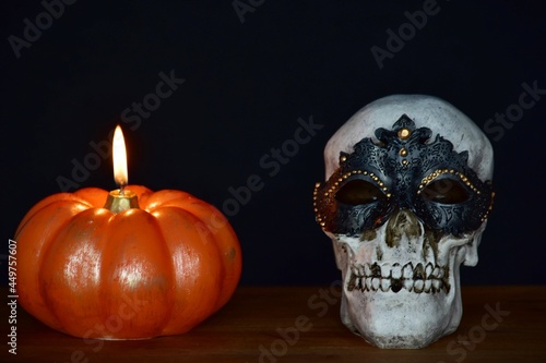 pumpkin candle and skull in mask on black background 
