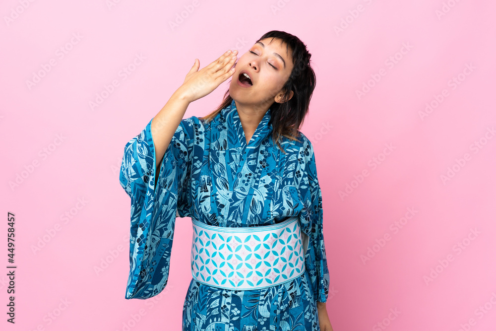 Young woman wearing kimono over isolated blue background yawning and covering wide open mouth with hand Young woman wearing kimono over isolated blue background yawning and covering wide open mouth with hand