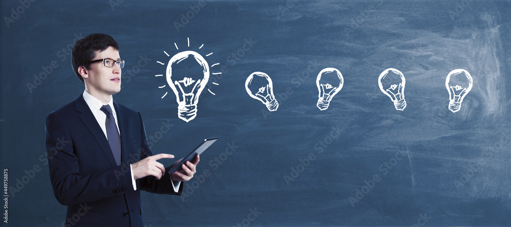 Attractive young european businessman with tablet standing on chalkboard wall background with lamp sketch. Idea, technology, solution and innovation concept. Attractive young european businessman with tablet standing on chalkboard wall background with lamp sketch. Idea, technology, solution and innovation concept.