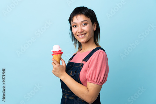 Young Uruguayan girl holding a cornet ice cream over isolated blue background smiling a lot