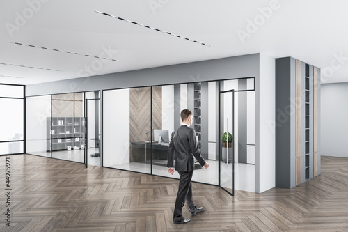 Businessperson walking in modern concrete glass office interior with daylight, equipment and wooden flooring. Workplace design concept.