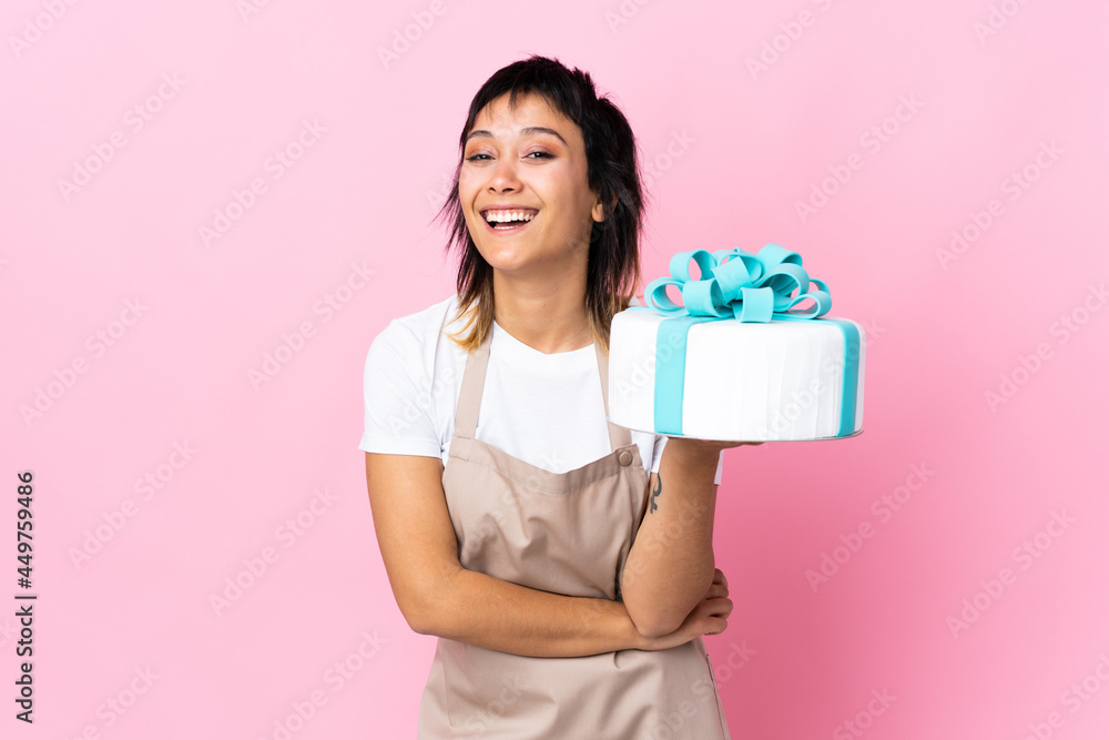 Uruguayan Pastry chef holding a big cake over isolated pink background laughing Uruguayan Pastry chef holding a big cake over isolated pink background laughing