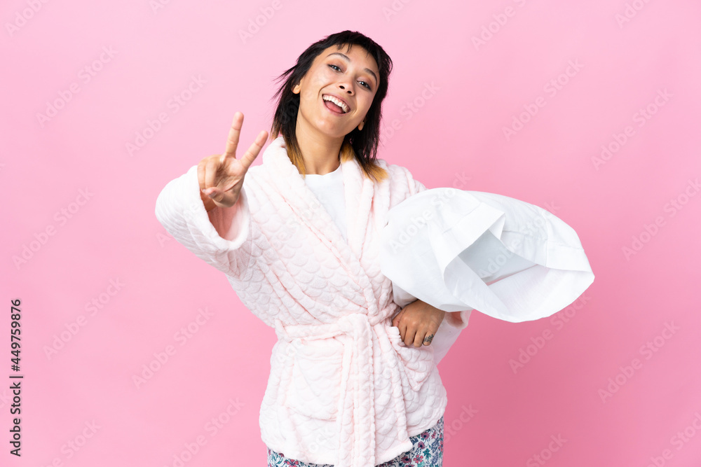 Young Uruguayan woman in pajamas over isolated pink background smiling and showing victory sign Young Uruguayan woman in pajamas over isolated pink background smiling and showing victory sign