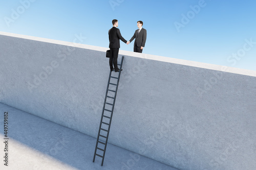 Happy businessmen on ladder shaking hands across concrete partition. Teamwork and success concept. photo