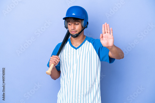 Baseball caucasian man player with helmet and bat isolated on blue background making stop gesture and disappointed