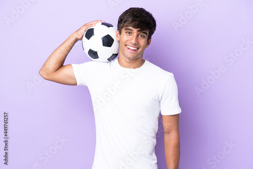 Young caucasian man isolated on purple background with soccer ball