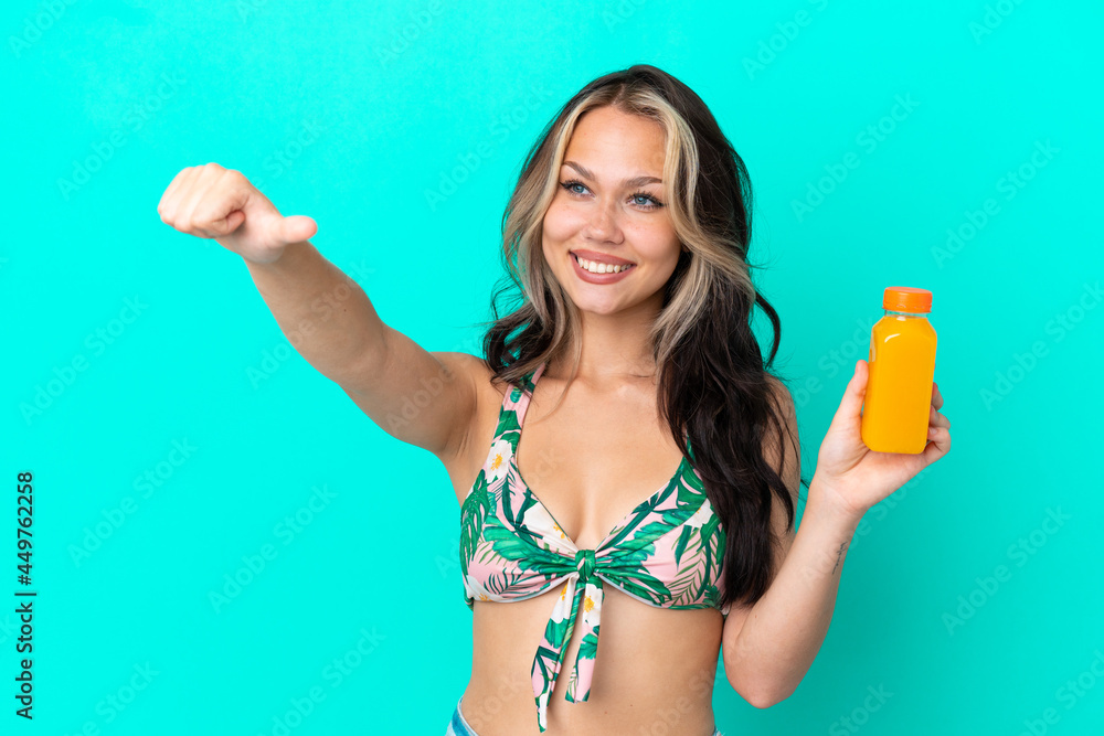 Teenager Russian girl in swimsuit drinking orange juice isolated on blue background giving a thumbs up gesture Teenager Russian girl in swimsuit drinking orange juice isolated on blue background giving a thumbs up gesture