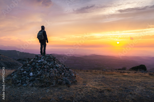 adventurous man on top of a mountain looking at a beautiful sunset. adventure travel