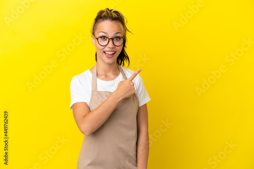 Restaurant waiter Russian girl isolated on yellow background surprised and pointing side