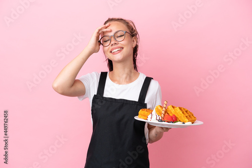Restaurant waiter Russian girl holding waffles isolated on pink background smiling a lot