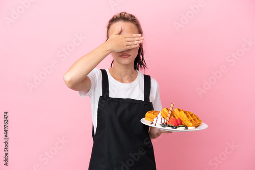 Restaurant waiter Russian girl holding waffles isolated on pink background covering eyes by hands. Do not want to see something