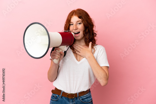 Teenager reddish woman isolated on pink background shouting through a megaphone with surprised expression