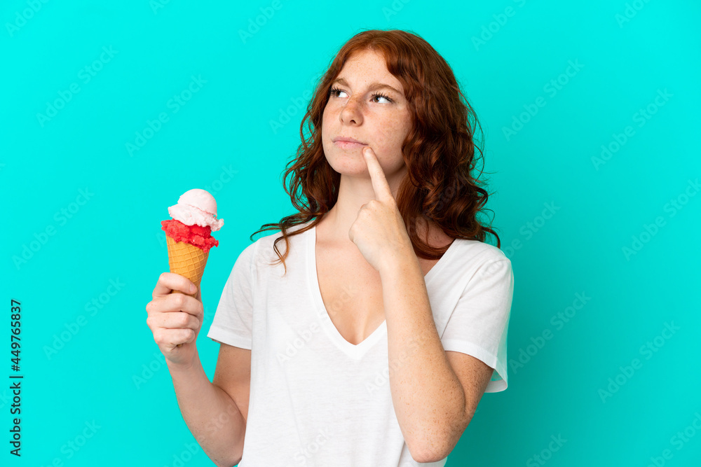 Teenager reddish woman with a cornet ice cream isolated on blue background having doubts while looking up Teenager reddish woman with a cornet ice cream isolated on blue background having doubts while looking up