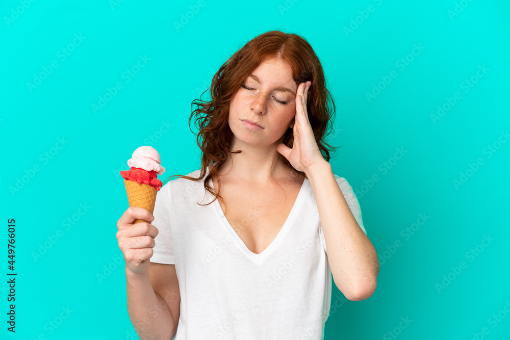 Teenager reddish woman with a cornet ice cream isolated on blue background with headache Teenager reddish woman with a cornet ice cream isolated on blue background with headache