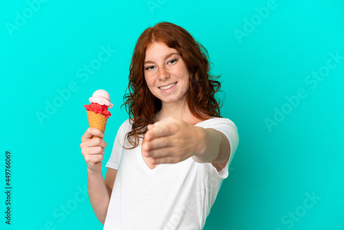 Teenager reddish woman with a cornet ice cream isolated on blue background shaking hands for closing a good deal