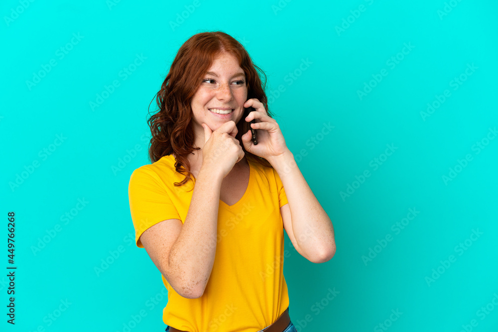 Teenager reddish woman using mobile phone isolated on blue background looking to the side and smiling Teenager reddish woman using mobile phone isolated on blue background looking to the side and smiling