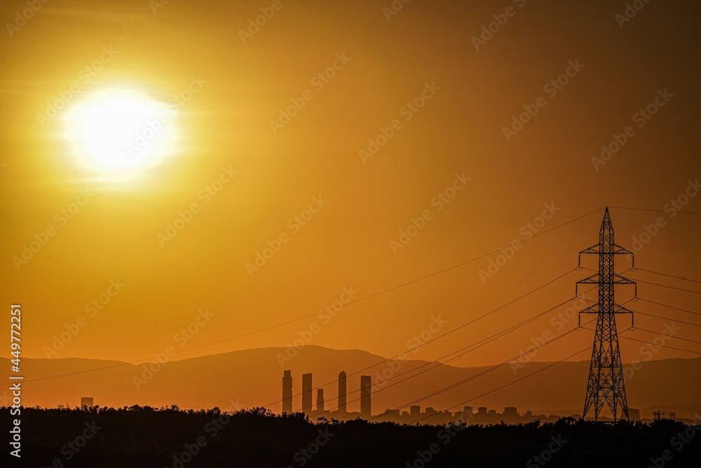 Horizontal image of the Madrid skyline in an orange sunset, with a high voltage electrical tower.