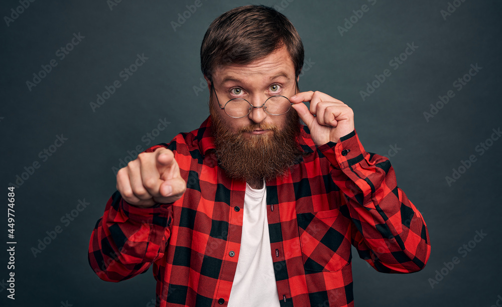 Portrait of a shocked bearded man in eyeglasses looking at camera isolated over grey background