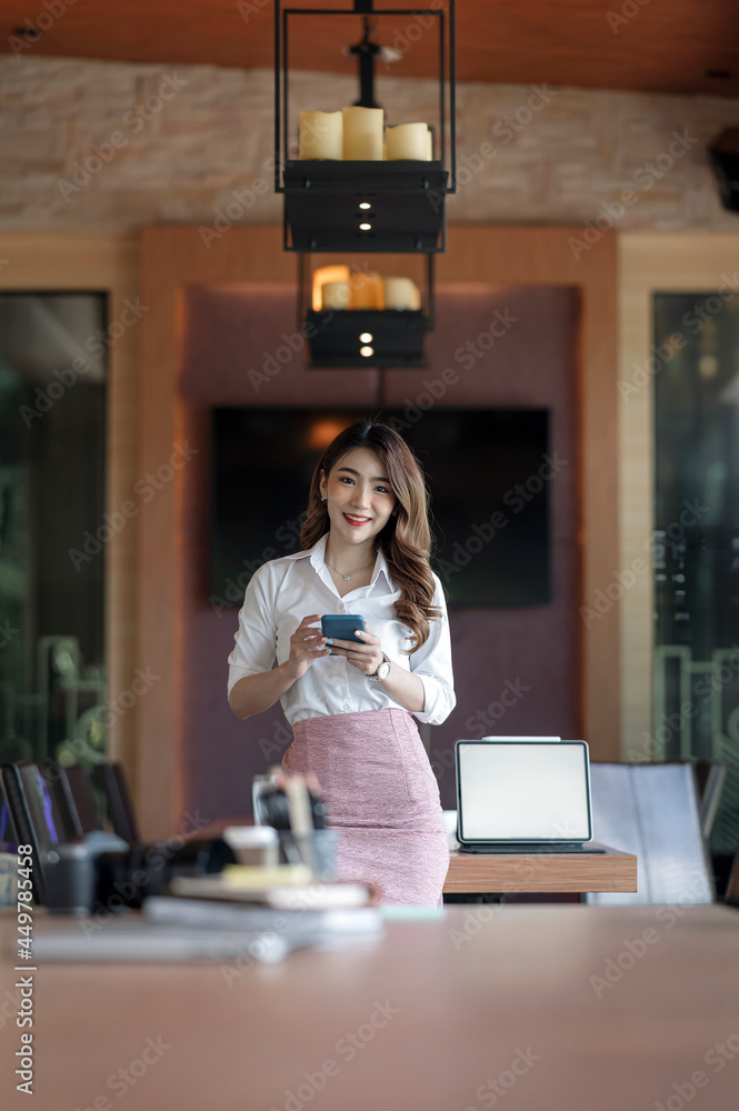 Portrait of young businesswoman using smartphone while standing in office room, vertical view. Portrait of young businesswoman using smartphone while standing in office room, vertical view.