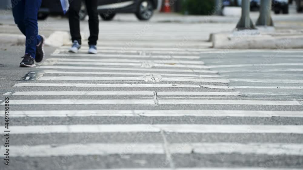 Pedestrians crossing a street by the crosswalk of a big city in daylight filmed in super slow motion in 4K high definition.