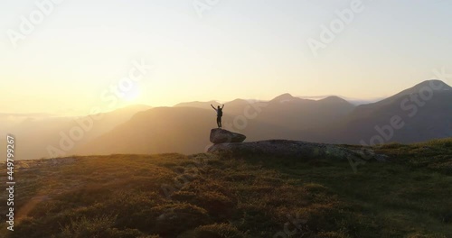 Norwegian hiker lifting arms cheering mountain climb in sunset - aerial orbit