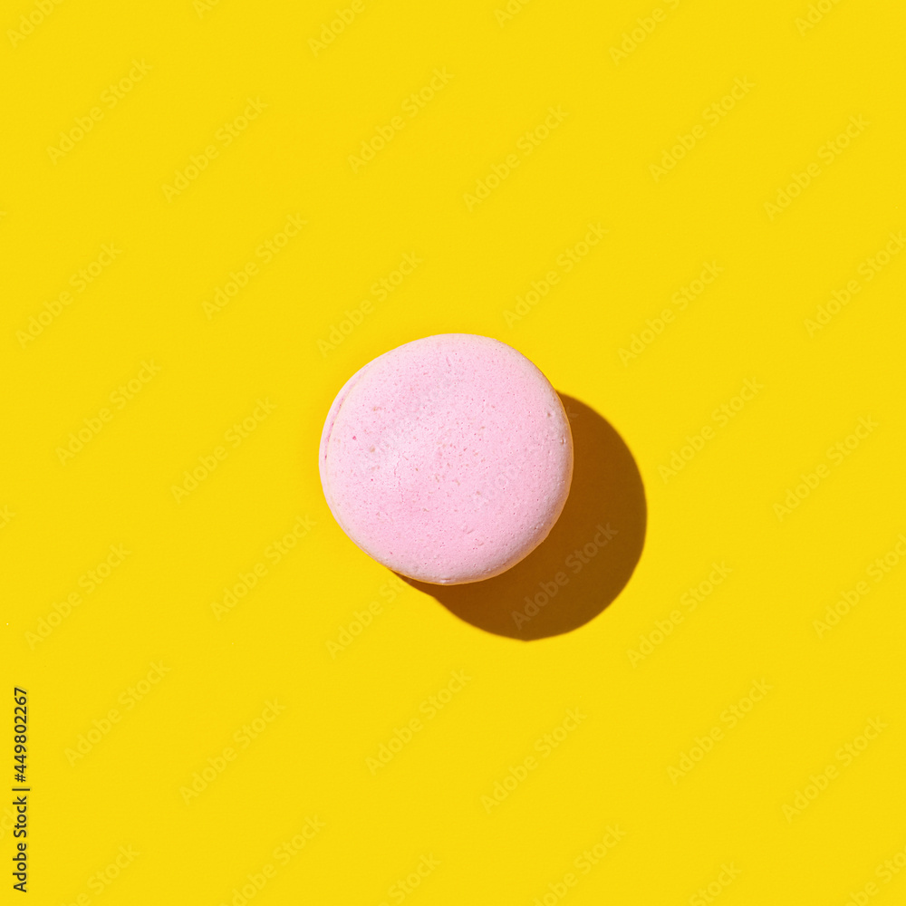 Obraz premium One pink macaroon on yellow colored background, colorful french cookie macaron.