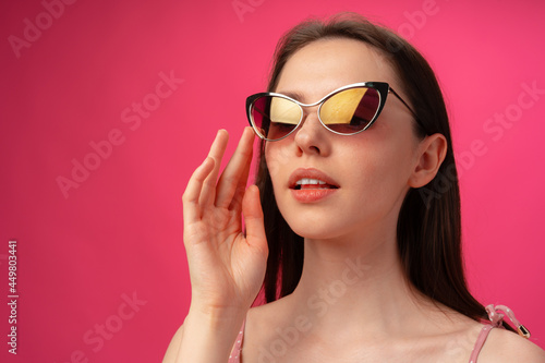 Young casual brunette woman in sunglasses against pink background