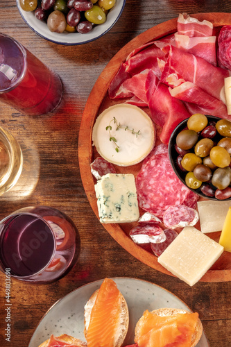 Wine, cheese, olives, charcuterie and salmon sandwiches. Delicious gourmet antipasti, shot from the top on a dark rustic wooden background, A bottle and glasses of wine, jamon, blue cheese