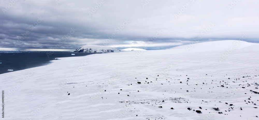 Obraz premium Panoramic view of the snowy lower slopes of Brown Bluff on the northern Antarctic peninsula. The landscape is strewn with basalt rock and the weather is cold and windy.
