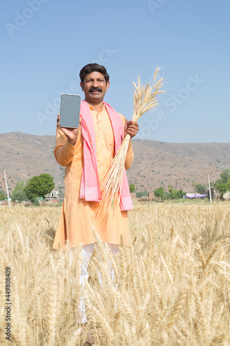 Happy rural farmer showing digital tablet in agriculture field photo