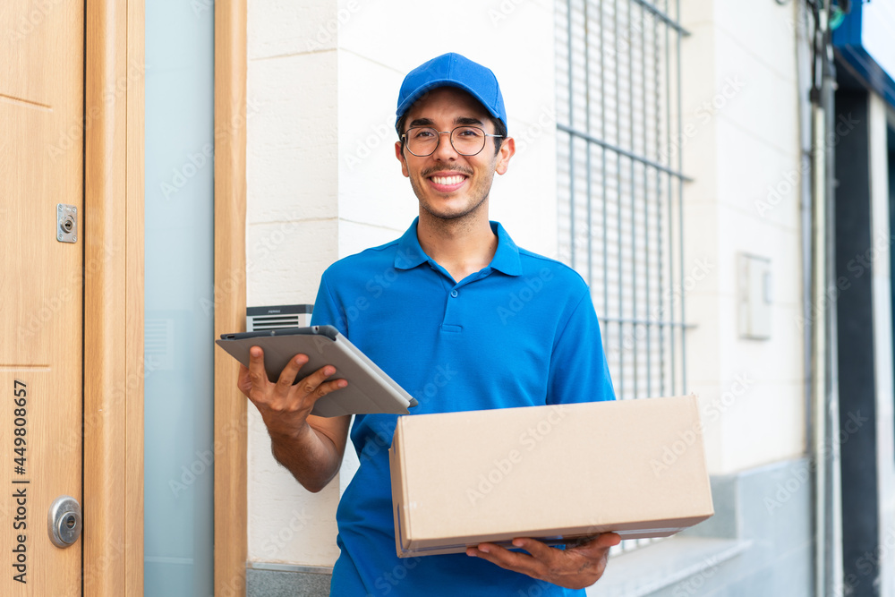 Young delivery man at outdoors holding boxes and a tablet with happy expression Young delivery man at outdoors holding boxes and a tablet with happy expression