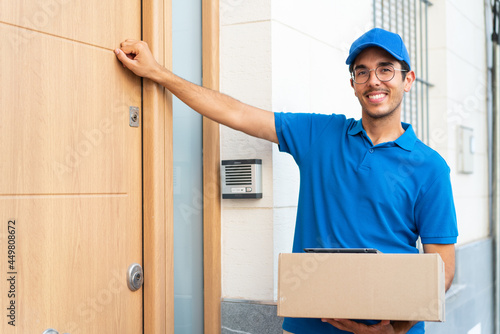Young delivery man at outdoors holding boxes and knocking on the door photo