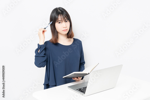 ノートパソコンを使いながら手帳にメモを書く若い女性 