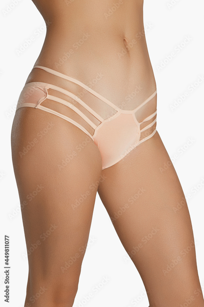 Cropped shot of slim lady in beige mesh panties with thin straps on the sides. The model is showing semi-opaque sexy lingerie on the gray background. Cropped shot of slim lady in beige mesh panties with thin straps on the sides. The model is showing semi-opaque sexy lingerie on the gray background.