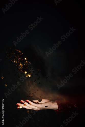 Christmas spirit. Festive background. Holiday decor. Female hands holding together opened palm throwing golden confetti spangles long exposure isolated black copy space.
