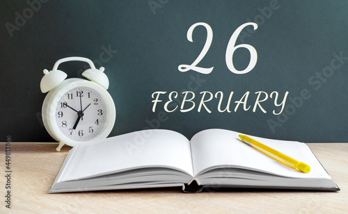 february 26. 26-th day of the month, calendar date.A white alarm clock, an open notebook with blank pages, and a yellow pencil lie on the table.Winter month, day of the year concept photo