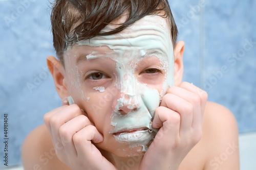 Portrait of child teen boy removing alginate mask from face looking at camera in bathroom at home. Spa beauty treatment. Teen problem skin, wellness, skincare and self love concept.