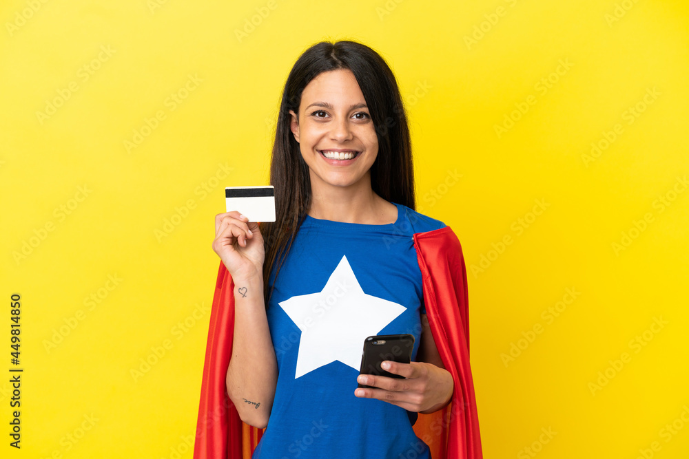 Super Hero woman isolated on yellow background buying with the mobile with a credit card Super Hero woman isolated on yellow background buying with the mobile with a credit card