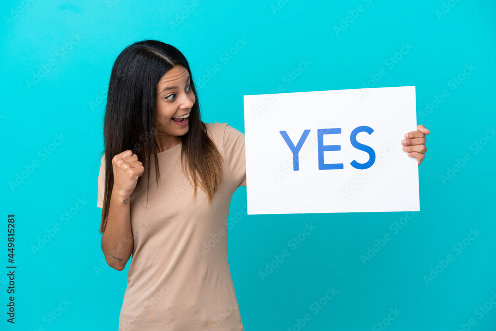 Young woman over isolated background holding a placard with text YES and celebration a victory Young woman over isolated background holding a placard with text YES and celebration a victory