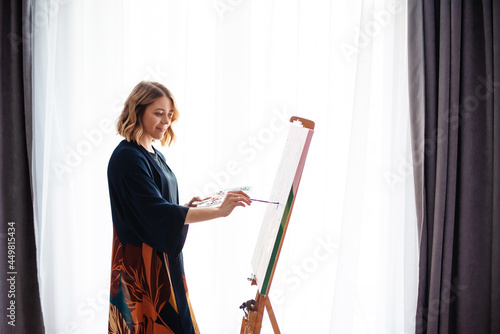 Creative woman painting on canvas near window