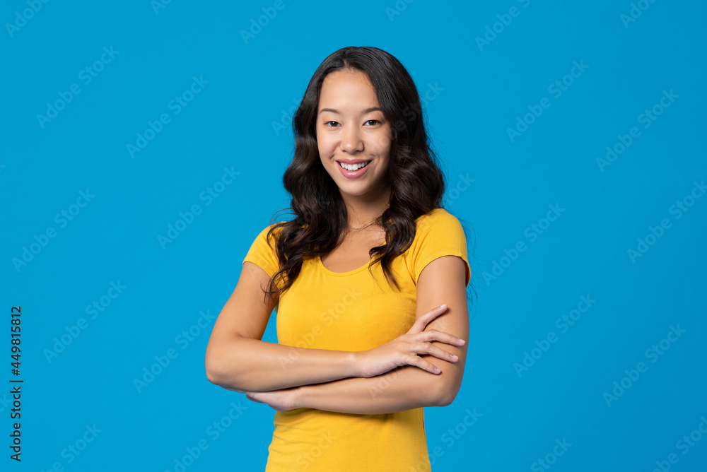 Smiling happy mixed race young millennial woman with arms crossed isolated on blue studio background Smiling happy mixed race young millennial woman with arms crossed isolated on blue studio background