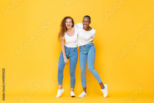 Happy two interracial woman friends smiling and holding each other in isolated studio yellow color background