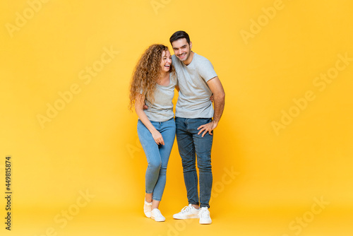 Full length portrait of young happy interracial millennial couple holding each other and laughing in isolated yellow studio background © Atstock Productions